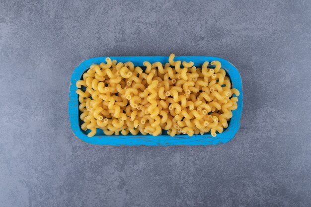 Maccheroni crudi del gomito sul piatto blu.