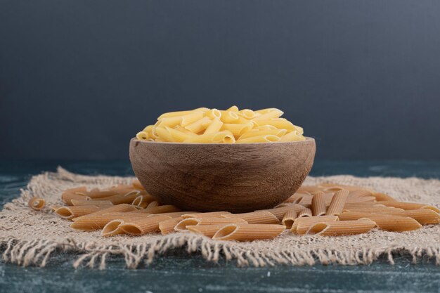 Maccheroni crudi freschi sulla ciotola di legno su tela da imballaggio.