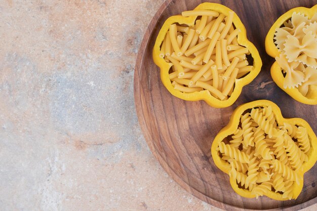 Maccheroni crudi su pepe su piatto di legno.