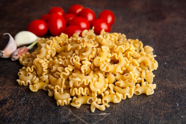 Maccheroni di vista dell'angolo alto con i pomodori e l'aglio su fondo strutturato scuro. orizzontale