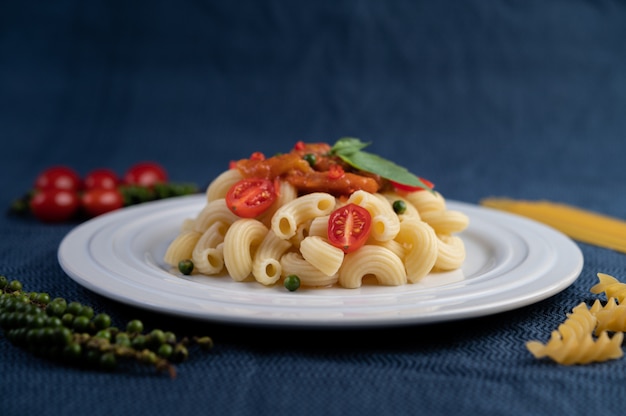 Maccheroni in padella con pomodoro, peperoncino, semi di pepe e basilico in un piatto bianco.