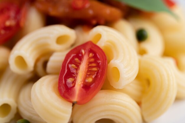 Maccheroni in padella con pomodoro, peperoncino, semi di pepe e basilico in un piatto bianco.