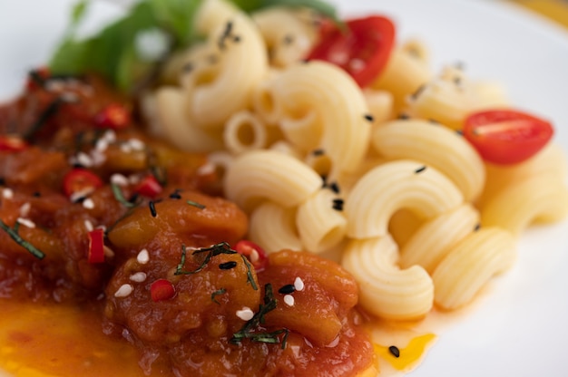 Maccheroni in padella con pomodoro, peperoncino, semi di pepe e basilico in un piatto bianco.