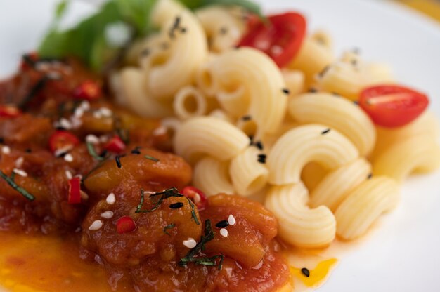 Maccheroni in padella con pomodoro, peperoncino, semi di pepe e basilico in un piatto bianco.