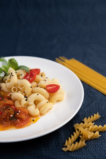 Maccheroni in padella con pomodoro, peperoncino, semi di pepe e basilico in un piatto bianco.