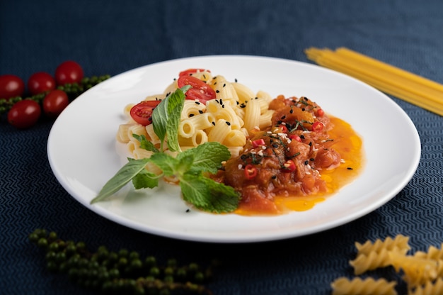 Maccheroni in padella con pomodoro, peperoncino, semi di pepe e basilico in un piatto bianco.