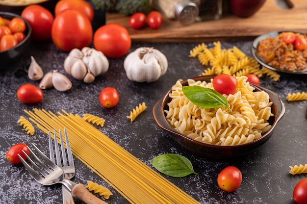 Maccheroni saltati con pomodori e basilico su un piatto grigio.