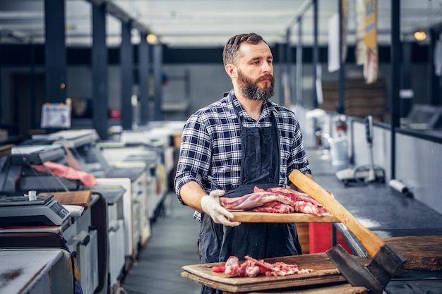 Macellaio barbuto vestito con una maglietta in pile che serve carne fresca tagliata in un mercato.