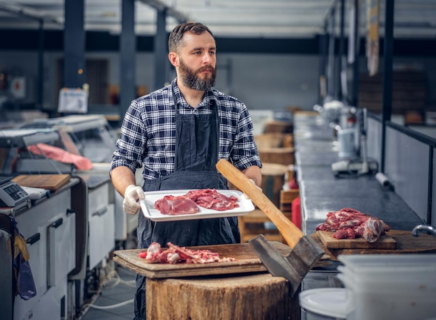 Macellaio barbuto vestito con una maglietta in pile che serve carne fresca tagliata in un mercato.