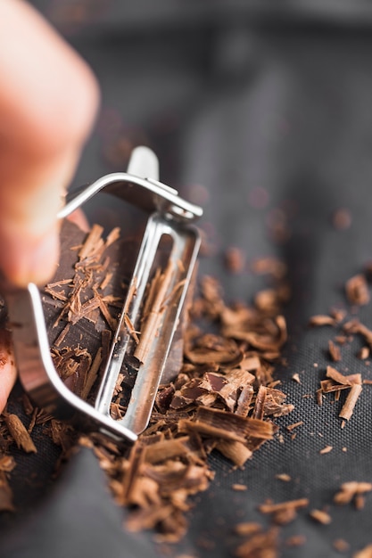 Macro colpo della mano della persona che rade la barra di cioccolato con lo sbucciatore