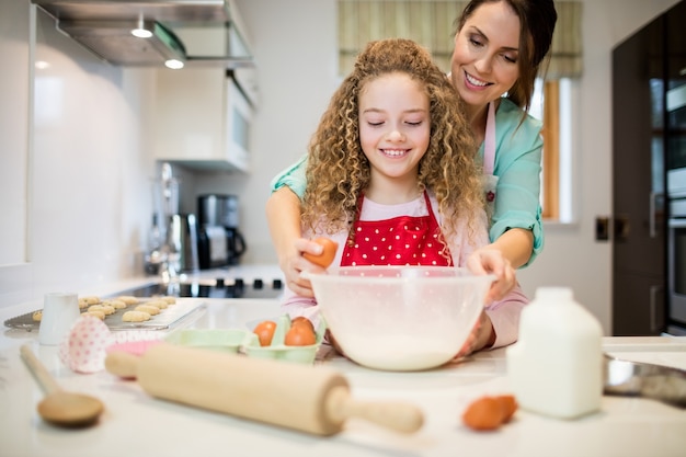 Madre aiutare la figlia a rompere le uova in cucina