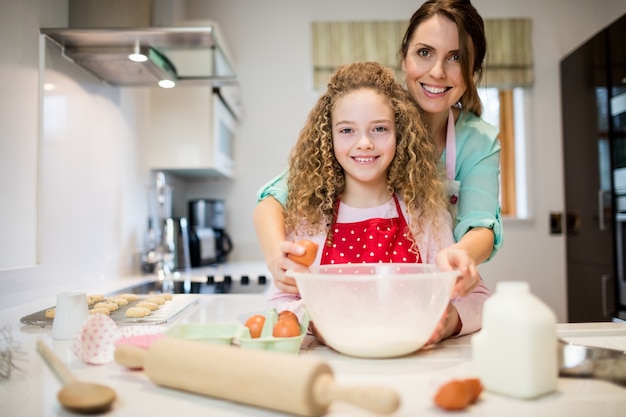 Madre aiutare la figlia a rompere le uova in cucina