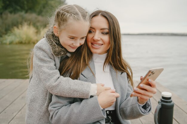 Madre alla moda con la figlia. Persone a un picnic. Donna in un cappotto grigio. Famiglia sull'acqua.