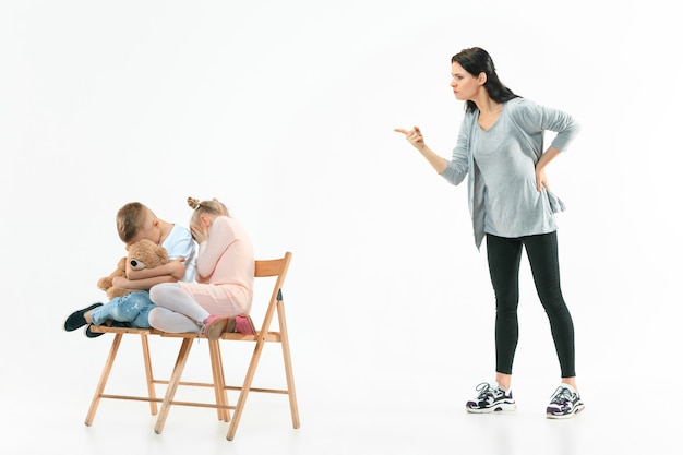 Madre arrabbiata che rimprovera suo figlio e sua figlia a casa. Studio shot di famiglia emotiva. Emozioni umane, infanzia, problemi, conflitti, vita domestica, concetto di relazione