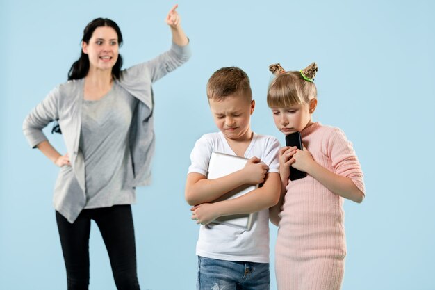 Madre arrabbiata che rimprovera suo figlio e sua figlia a casa. Studio shot di famiglia emotiva. Emozioni umane, infanzia, problemi, conflitti, vita domestica, concetto di relazione