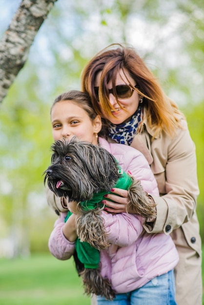 Madre che abbraccia sua figlia e cane all&#39;aperto