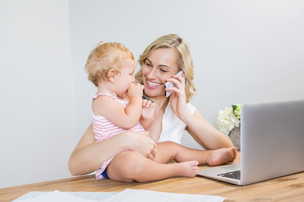 Madre che comunica sul telefono cellulare mentre si tiene la sua neonata