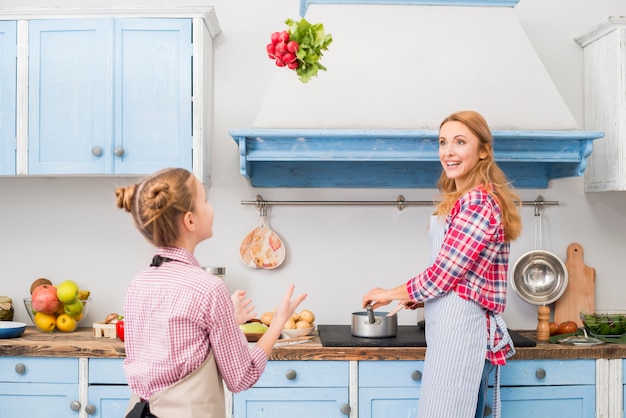 Madre che cucina cibo guardando sua figlia che getta ravanello in aria in cucina