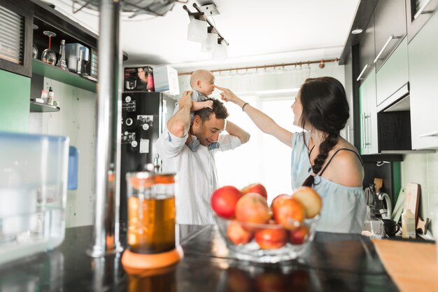 Madre che punta il dito sul naso del bambino seduto sulla spalla dell&#39;uomo in cucina