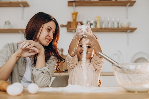 Madre con figlia che gioca con la farina e cuoce in cucina