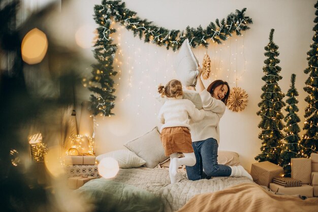 Madre con figlia che si diverte con i cuscini sul letto a Natale