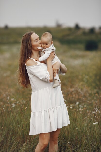 Madre con figlia. Famiglia in un campo. Ragazza appena nata. Donna in abito bianco.