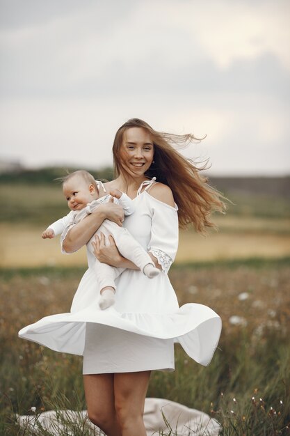 Madre con figlia. Famiglia in un campo. Ragazza appena nata. Donna in abito bianco.