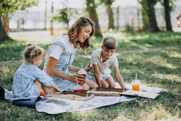 Madre con figlio e figlia che mangiano pizza nel parco