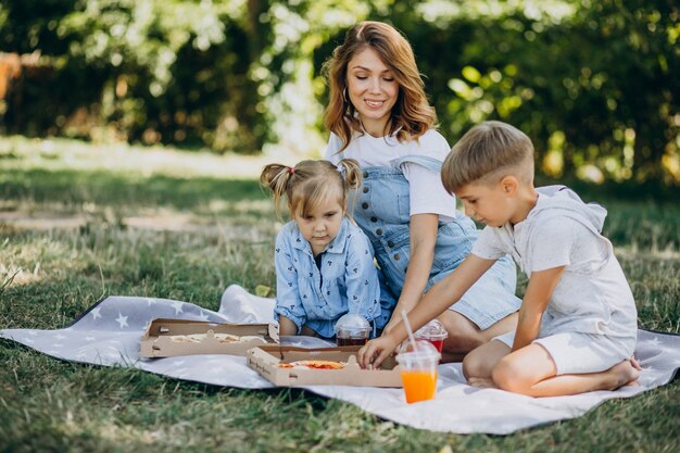 Madre con figlio e figlia che mangiano pizza nel parco