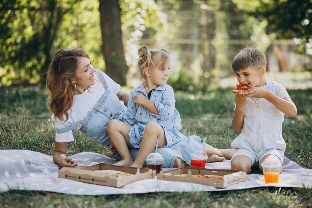 Madre con figlio e figlia che mangiano pizza nel parco