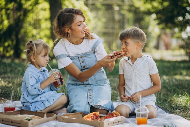 Madre con figlio e figlia che mangiano pizza nel parco