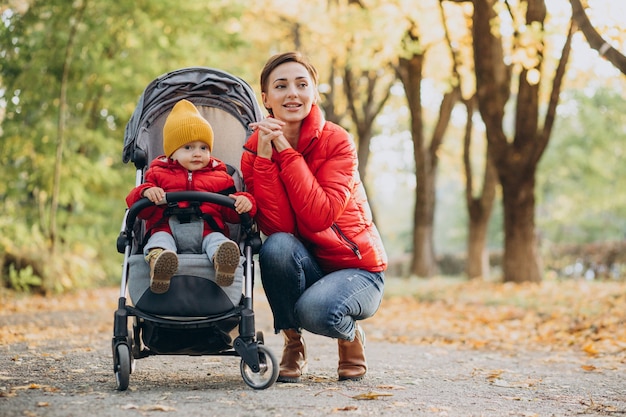 Madre con figlio piccolo nel passeggino che cammina nel parco autunnale