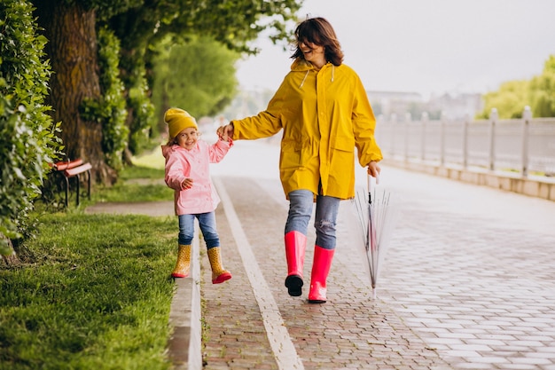 Madre con la figlia che cammina nel parco sotto la pioggia che indossa stivali di gomma