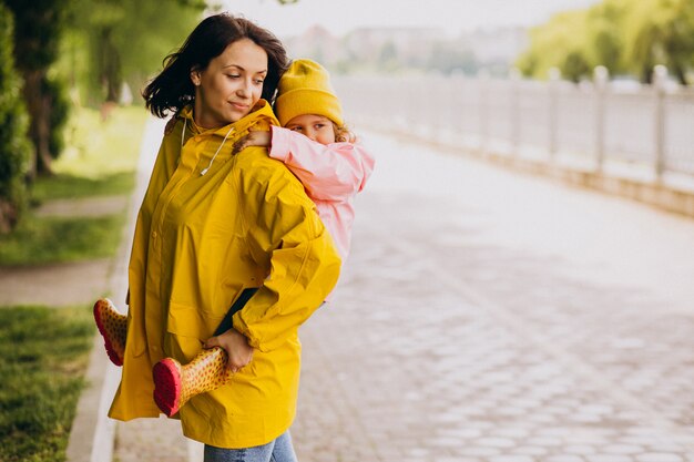 Madre con la figlia che cammina nel parco sotto la pioggia che indossa stivali di gomma