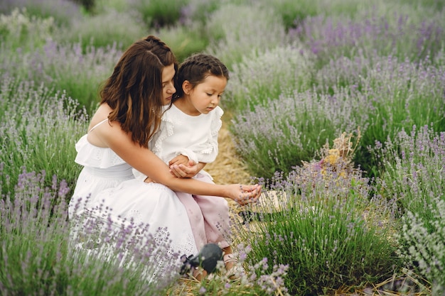 Madre con la piccola figlia sul campo di lavanda. Bella donna e bambino sveglio che giocano nel campo del prato. Vacanze in famiglia in una giornata estiva.