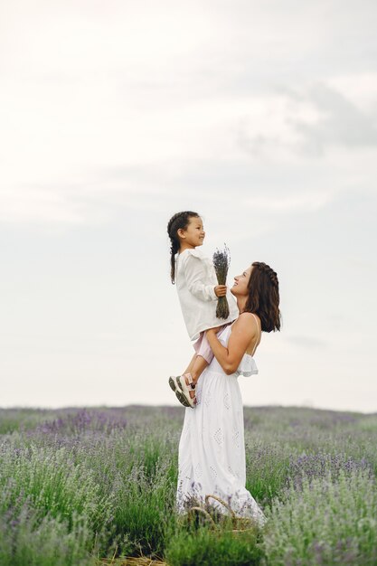 Madre con la piccola figlia sul campo di lavanda. Bella donna e bambino sveglio che giocano nel campo del prato. Vacanze in famiglia in una giornata estiva.