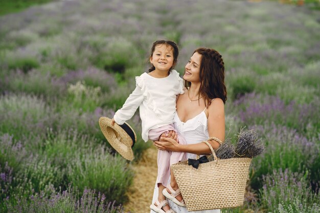 Madre con la piccola figlia sul campo di lavanda. Bella donna e bambino sveglio che giocano nel campo del prato. Vacanze in famiglia in una giornata estiva.