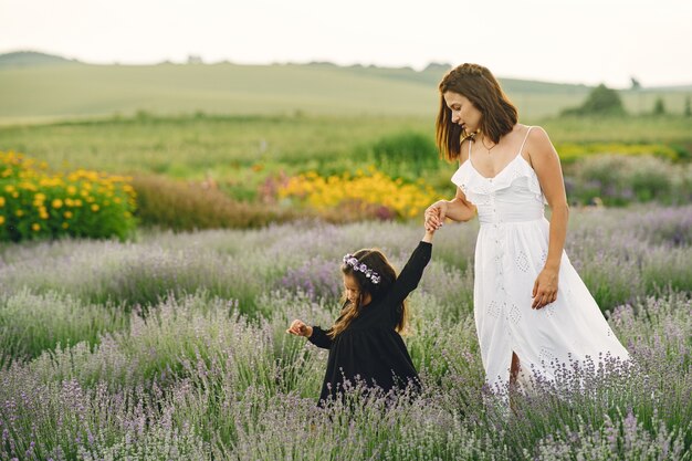 Madre con la piccola figlia sul campo di lavanda. Bella donna e bambino sveglio che giocano nel campo del prato. Vacanze in famiglia in una giornata estiva.