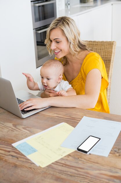Madre con laptop con bambino in cucina