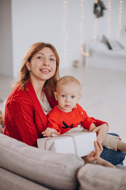 Madre con suo figlio bambino seduto sul divano e disimballaggio regali di Natale