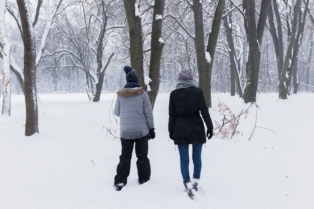 Madre di retrovisione con sua figlia che cammina nella foresta al giorno di inverno