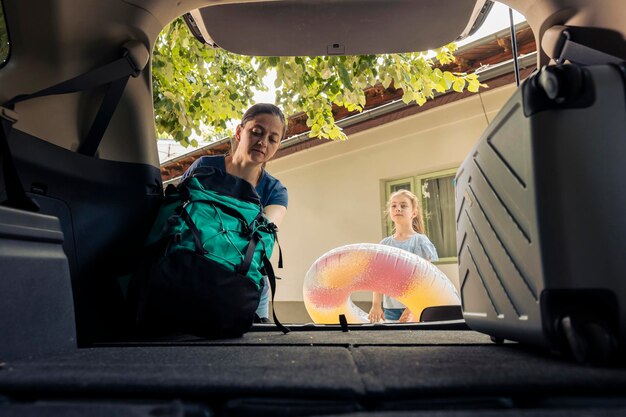 Madre e bambina che caricano i bagagli nel bagagliaio dell'auto, in viaggio per le vacanze estive. Mettere gonfiabili e borse da viaggio in automobile per partire in vacanza avventurosa al mare.