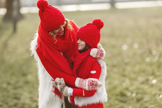 Madre e bambino in cappelli invernali lavorati a maglia in vacanza di Natale in famiglia. Cappello e sciarpa in lana fatti a mano per mamma e bambino. Lavoro a maglia per bambini. Capispalla in maglia. Donna e bambina in un parco.