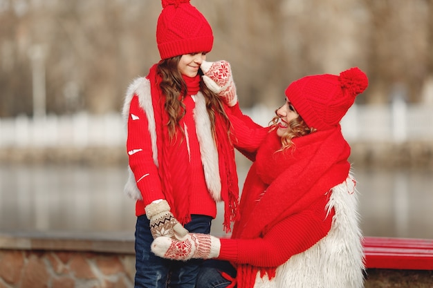 Madre e bambino in cappelli invernali lavorati a maglia in vacanza di Natale in famiglia. Cappello e sciarpa in lana fatti a mano per mamma e bambino. Lavoro a maglia per bambini. Capispalla in maglia. Donna e bambina in un parco.