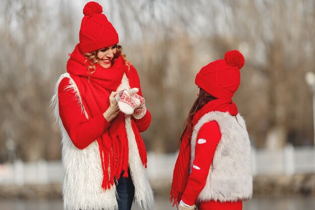 Madre e bambino in cappelli invernali lavorati a maglia in vacanza di Natale in famiglia. Cappello e sciarpa in lana fatti a mano per mamma e bambino. Lavoro a maglia per bambini. Capispalla in maglia. Donna e bambina in un parco.