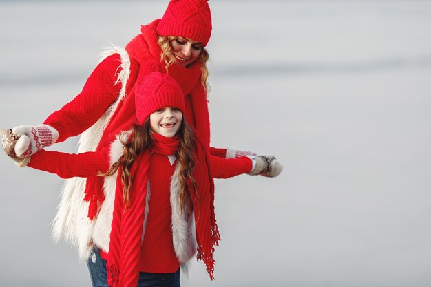 Madre e bambino in cappelli invernali lavorati a maglia in vacanza di Natale in famiglia. Cappello e sciarpa in lana fatti a mano per mamma e bambino. Lavoro a maglia per bambini. Capispalla in maglia. Donna e bambina in un parco.