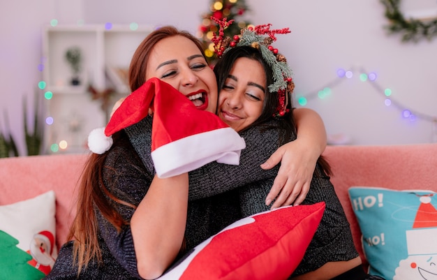 Madre e figlia amorevole si abbracciano seduti sul divano godendosi il periodo natalizio a casa