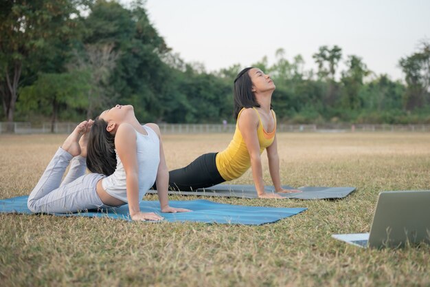 Madre e figlia che fanno yoga. formazione donna e bambino nel parco. sport all'aperto. stile di vita sportivo sano, guardare video tutorial online di esercizi di yoga e allungare il torace e la colonna vertebrale.