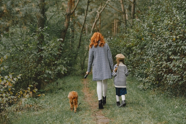 Madre e figlia che giocano con il cane. Famiglia nella sosta di autunno. Pet, animali domestici e concetto di stile di vita. Tempo d'autunno.