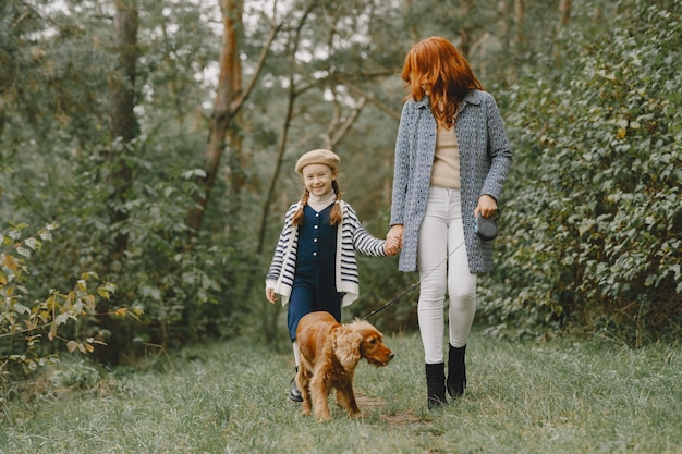 Madre e figlia che giocano con il cane. Famiglia nella sosta di autunno. Pet, animali domestici e concetto di stile di vita. Tempo d'autunno.